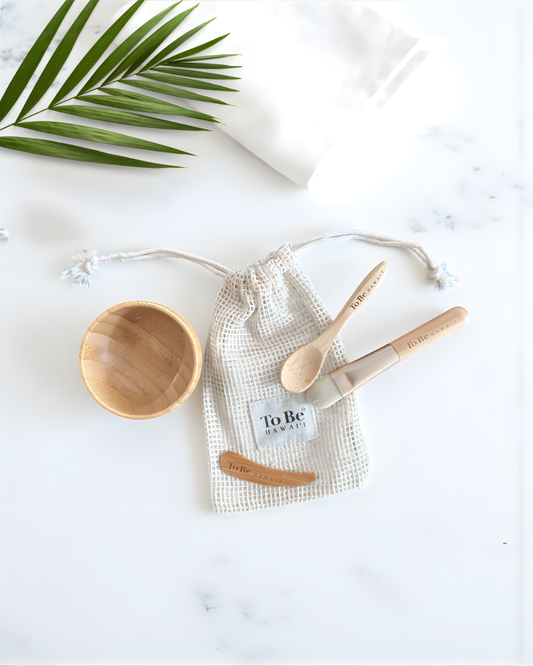 Wooden bowl, spoon, and small bag with 'To Be' branding on a white surface with a palm leaf.