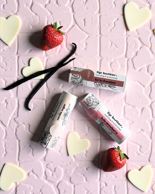 Three lip butter products on a pink textured background with strawberries and vanilla beans.