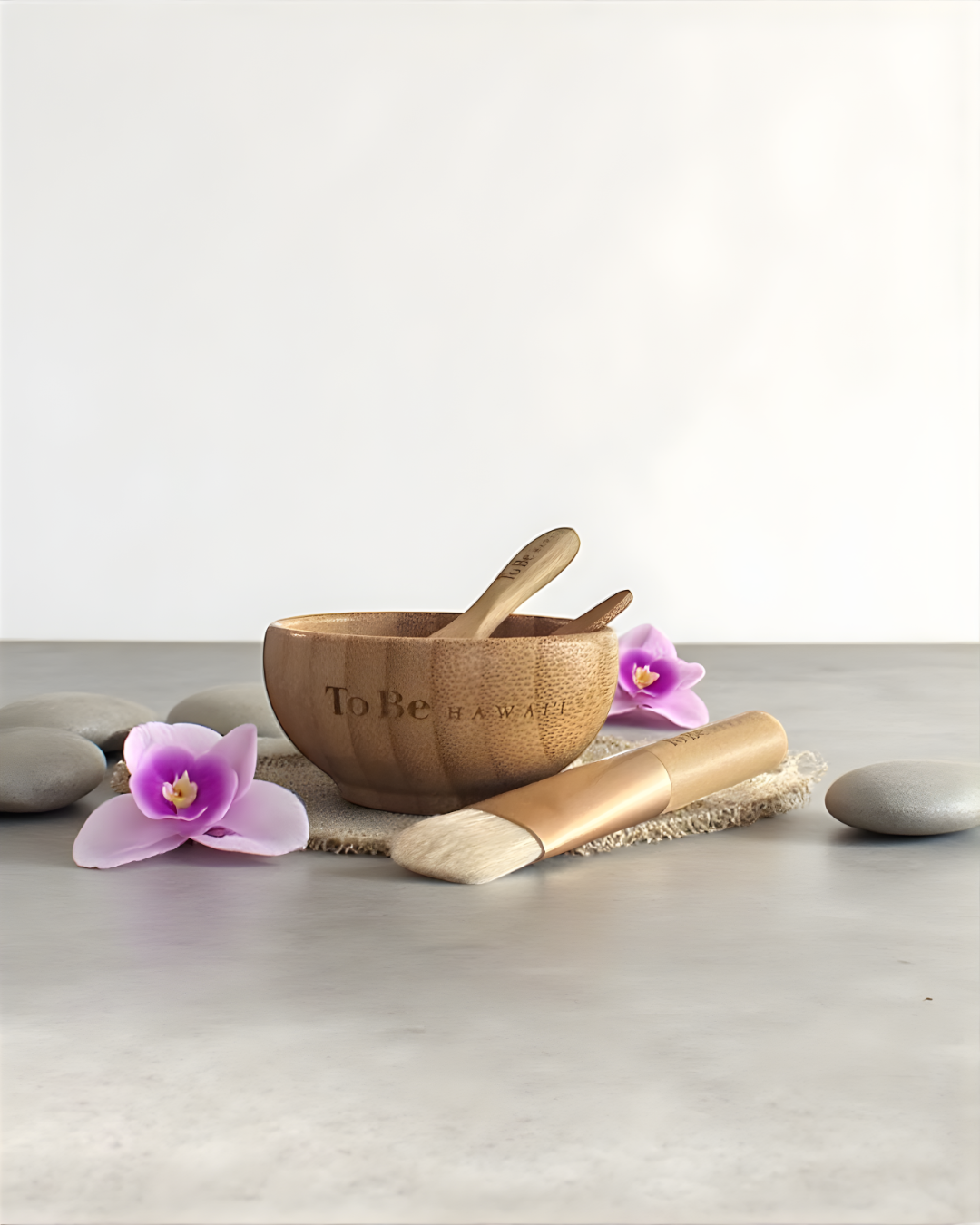 Wooden bowl with a spoon, brush, and purple orchids on a light surface.