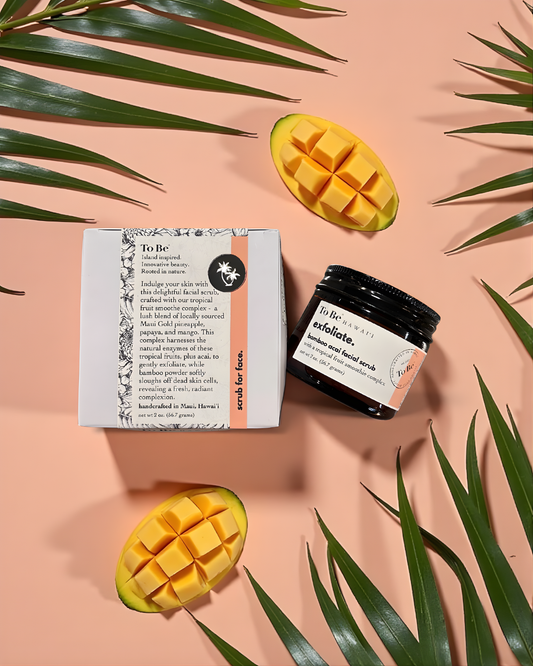 Exfoliating product with packaging and mango slices on a pink background with green leaves.