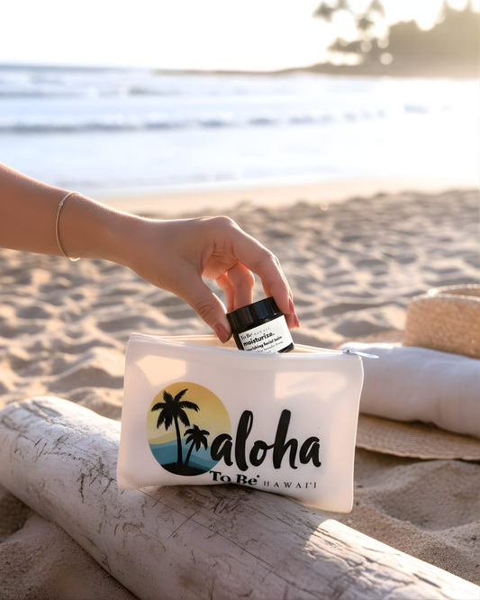 Person holding a travel facial balm jar over a zip pouch with 'aloha' text on a beach.