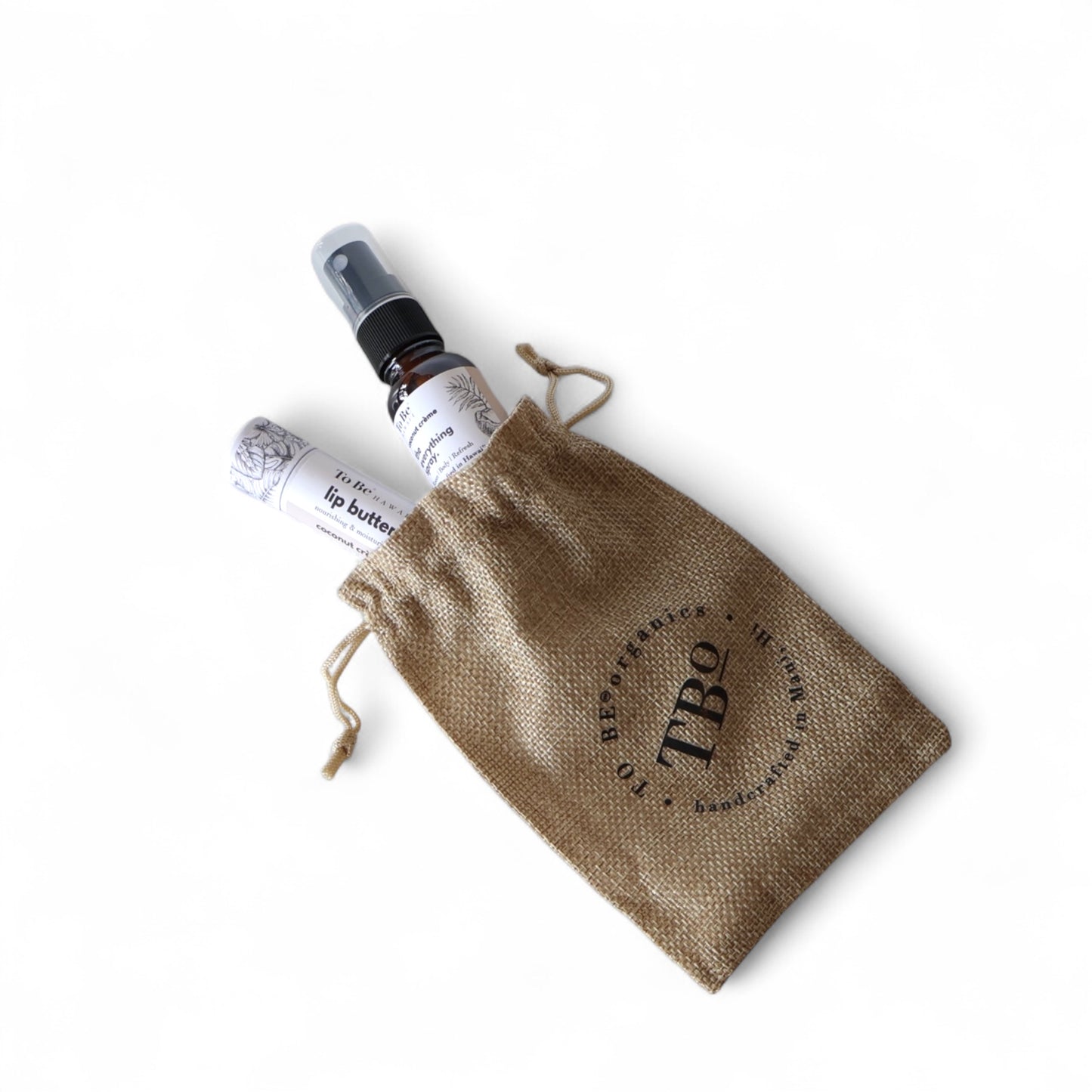 a small everything spray bottles and a lip butter in a burlap drawstring bag with 'TBO' branding.
