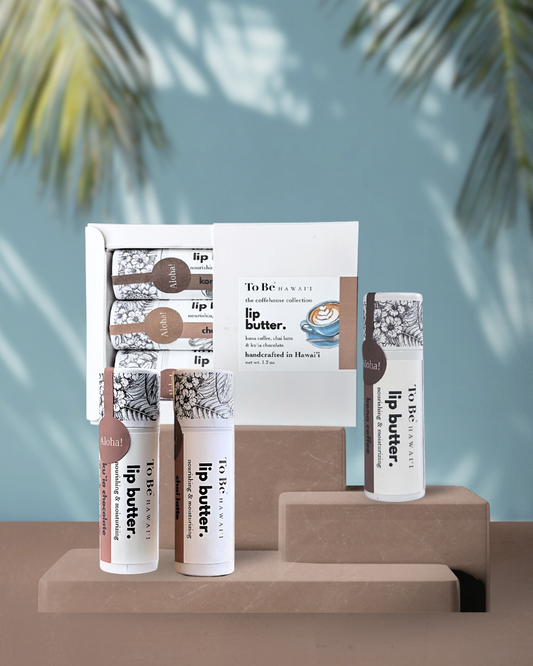Three lip butters, Kona coffee, kuia chocolate and chai latte, packaged in a white gift box on a brown surface.