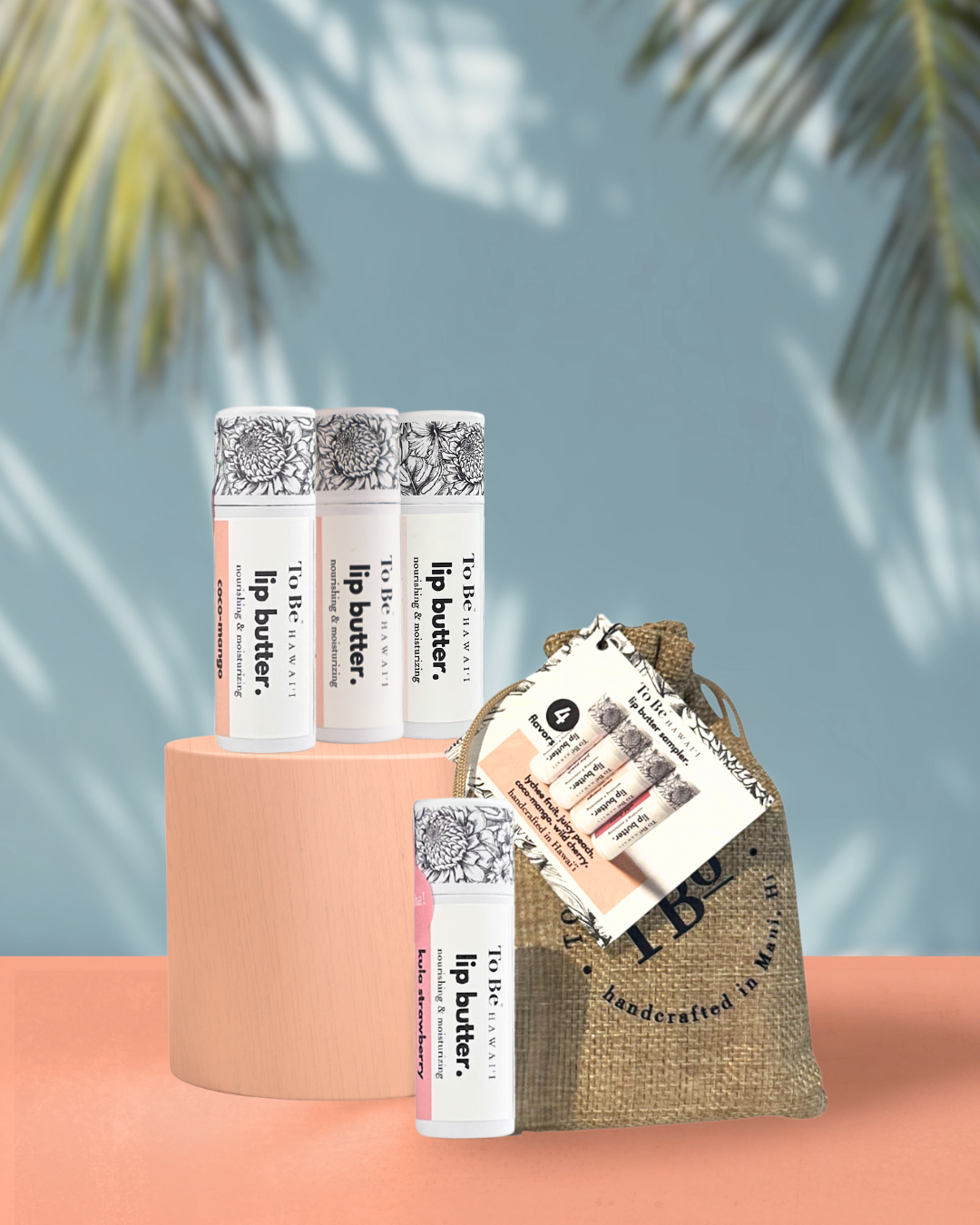 Four lip butters coco-mango, lychee fruit, guava nectar, and kula strawberry with a burlap bag with a drawstring on a orange colored surface.