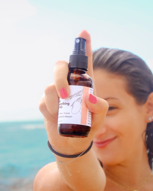 Person holding a brown spray bottle with a label against a blurred beach background