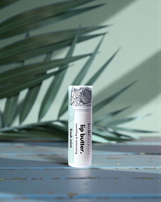 Fresh Mint  Lip butter in a cardboard push up recyclable tube on a blue surface with green leaves in the background