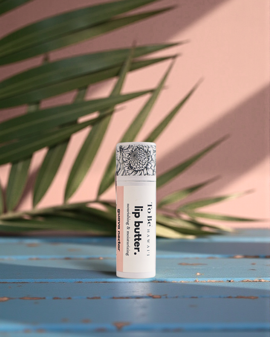 Guava Nectar  Lip butter in a cardboard push up recyclable tube on a blue surface with green leaves in the background