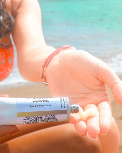 Person applying velvet hand & body butter on a beach