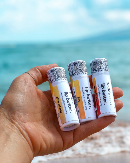 Hand holding lip butter tubes with a beach background