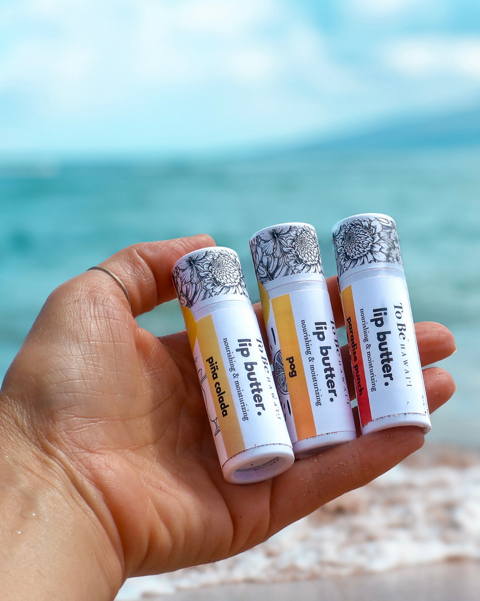 Hand holding lip butter tubes with a beach background