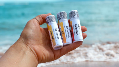 Hand holding three lip butter tubes with a beach background