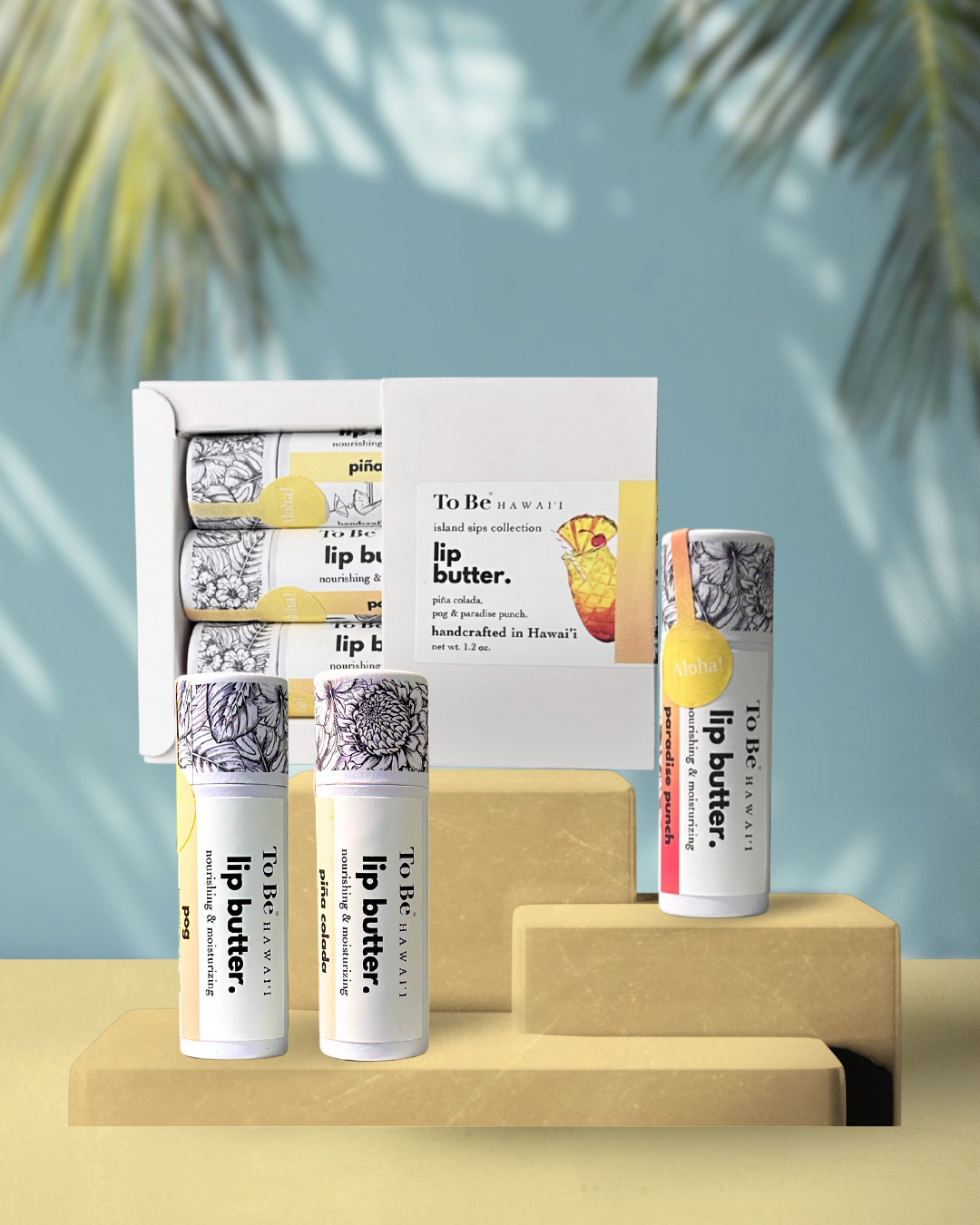 three lip butter gift set. Paradise punch, pina colada, and P.O.G. lip butters packaged in a white box on a yellow surface.