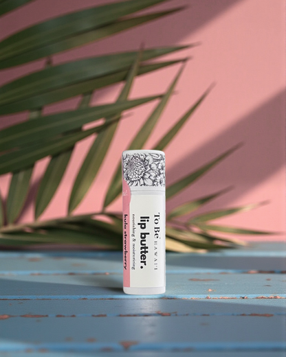 Kula Strawberry  Lip butter in a cardboard push up recyclable tube on a blue surface with green leaves in the background