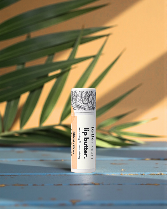 Lilikoi citrus Lip butter in a cardboard push up recyclable tube on a blue surface with green leaves in the background