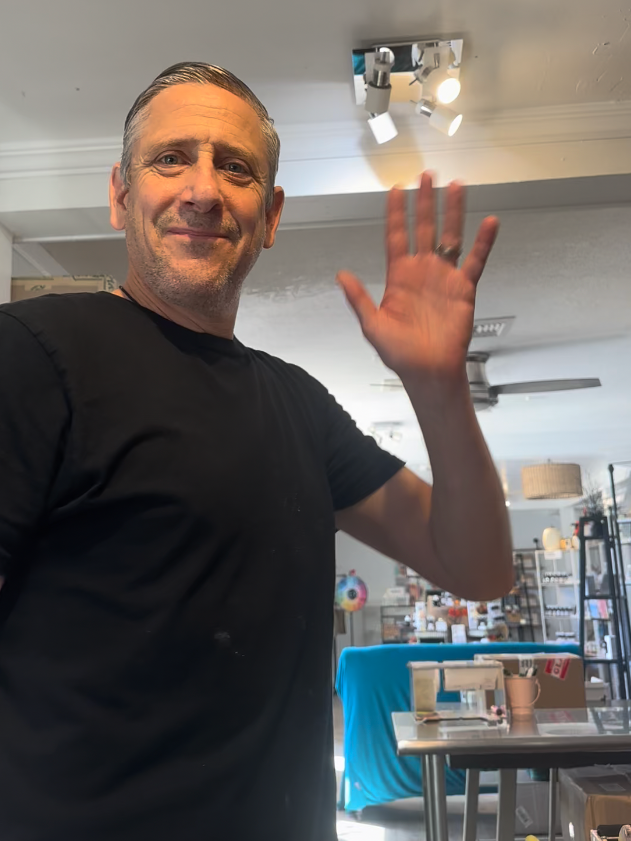 Man waving in a store setting with shelves and products in the background