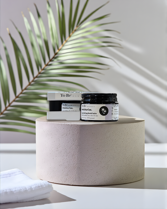 To Be Facial Balm products on a round stone surface with a plant in the background