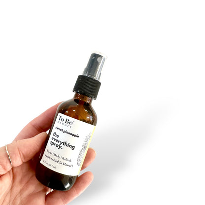 A hand holding a bottle of 'The Everything Spray, Sweet Pineapple' with a fine mister, written on the label.