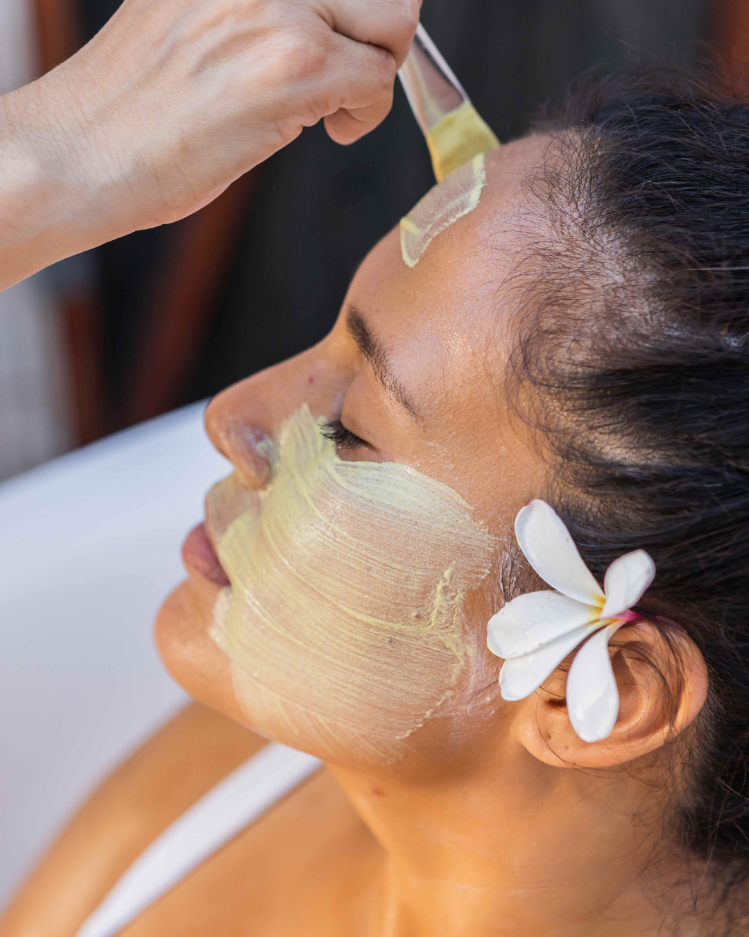 Person applying the pineapple  facial mask to their face with a flower in their hair.