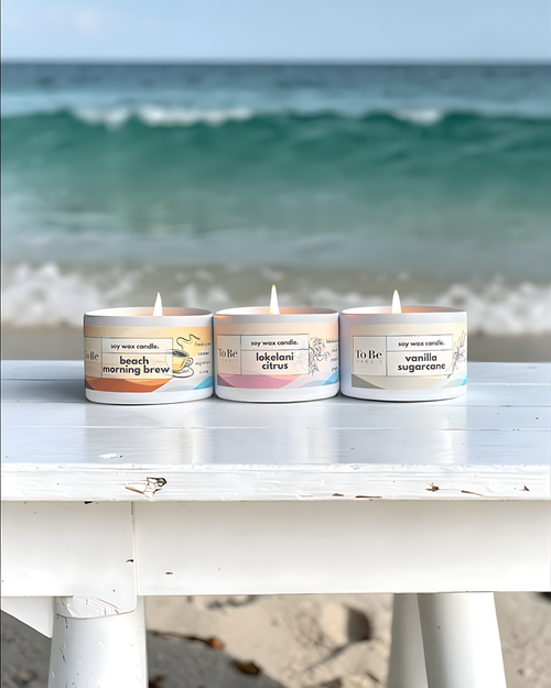 Three candles with labels on a white surface with ocean waves in the background