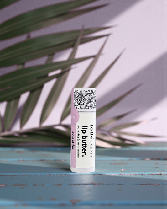 Sweet Fig Lip butter in a cardboard push up recyclable tube on a blue surface with green leaves in the background