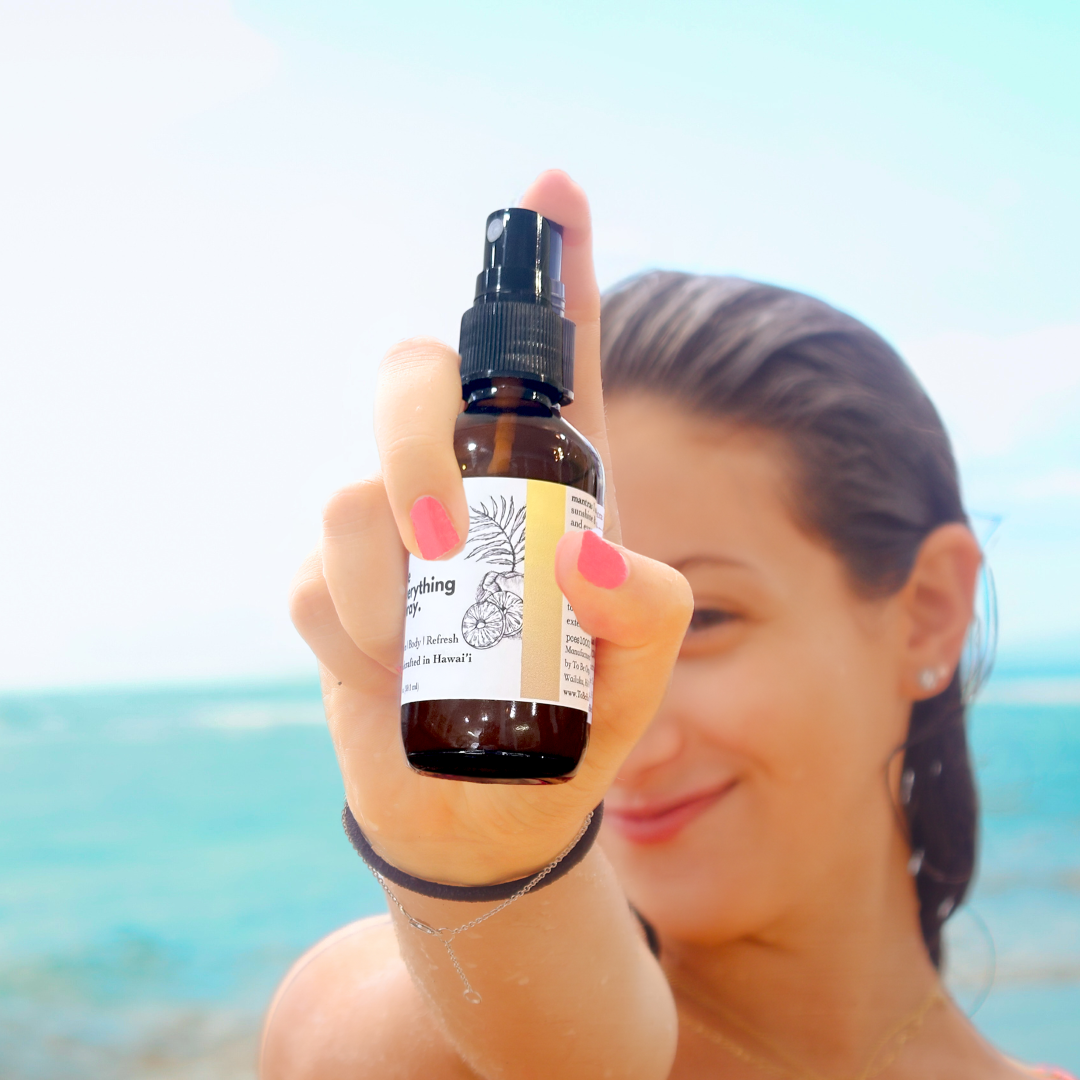 Person holding a bottle of Everything room & body spray with a beach in the background