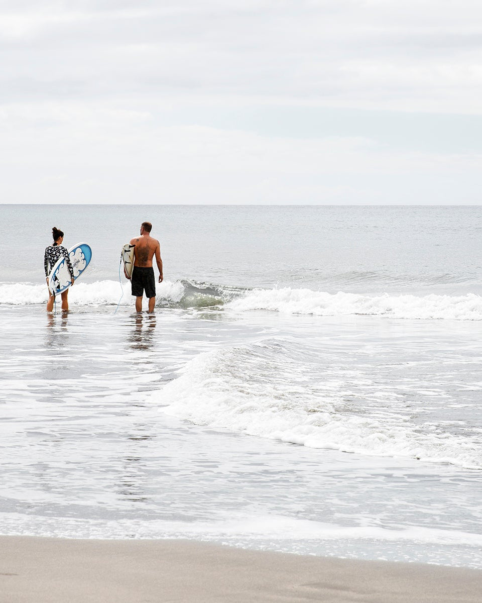 A man and a woman entering the ocean with their surfboards