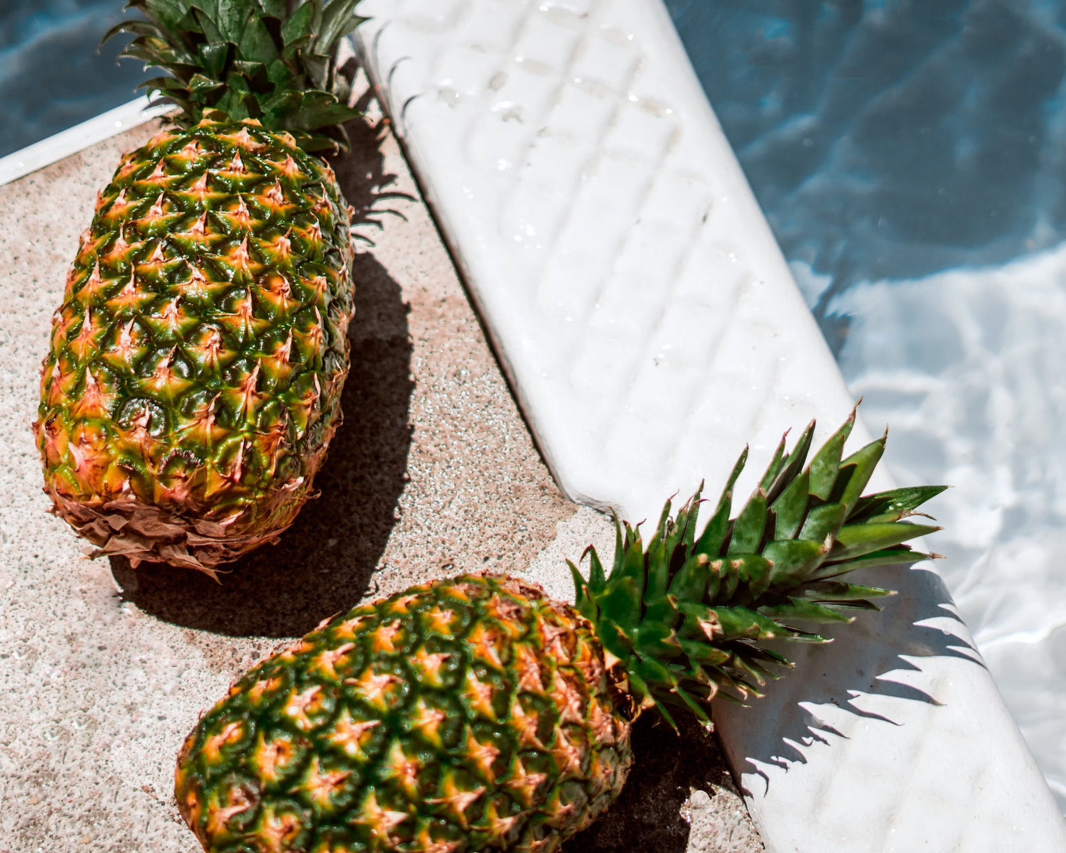 2 fresh pineapples laying by the pool in the sunshine